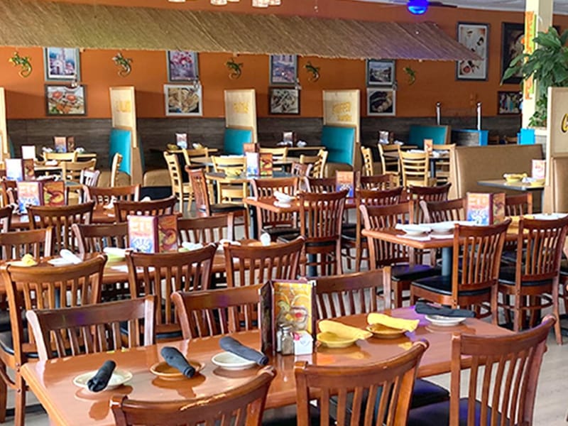 Dining room at Chavez Mexican Cafe with wooden chairs, tables set with yellow napkins, and orange walls hung with framed photos.