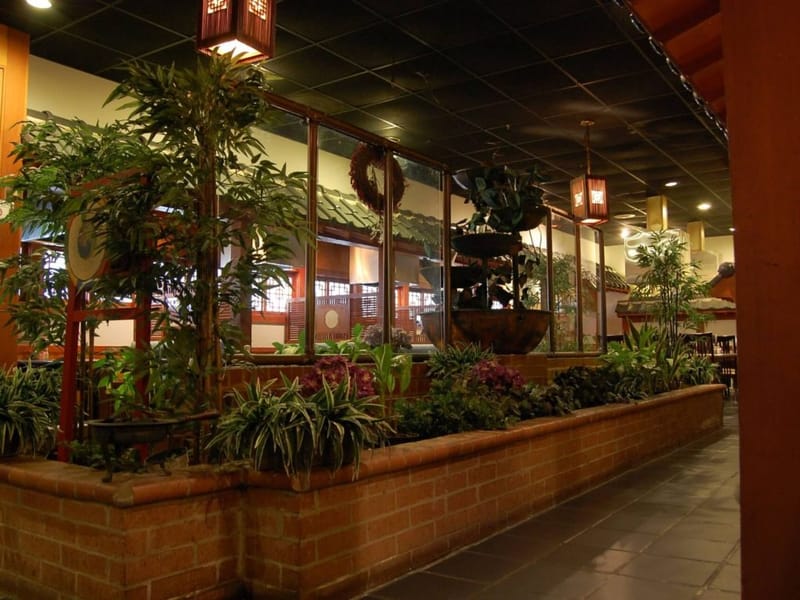 Interior of Korea Garden Korean restaurant in Spring Branch, with a brick planter wall, leafy plants, a tiered fountain, and hanging lanterns.