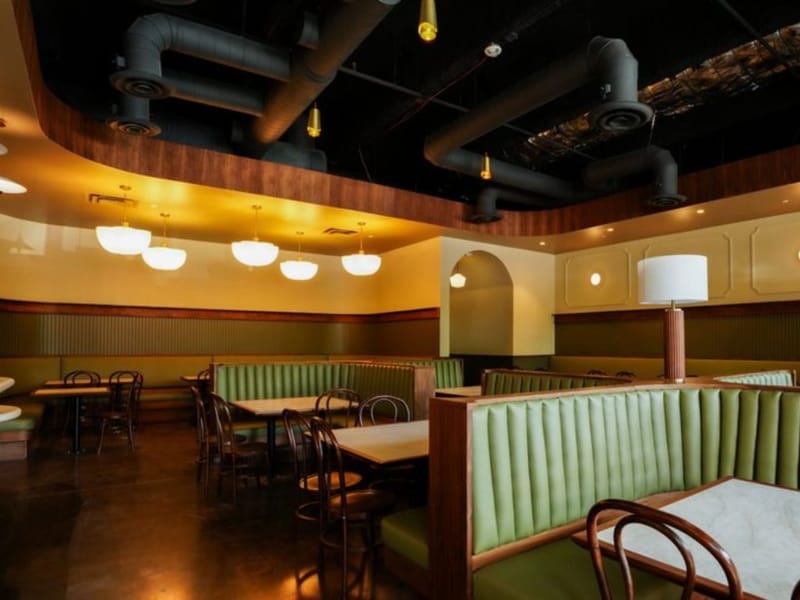 Dining room at Murray's Pizza & Wine with green tufted banquette booths, marble-topped tables, and schoolhouse pendant lights.