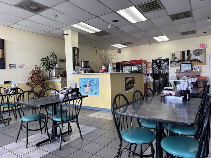 Casual dining room at Pho Luc Lac in Spring Branch, with teal-cushioned chairs, a yellow service counter, and a bubble tea sign.